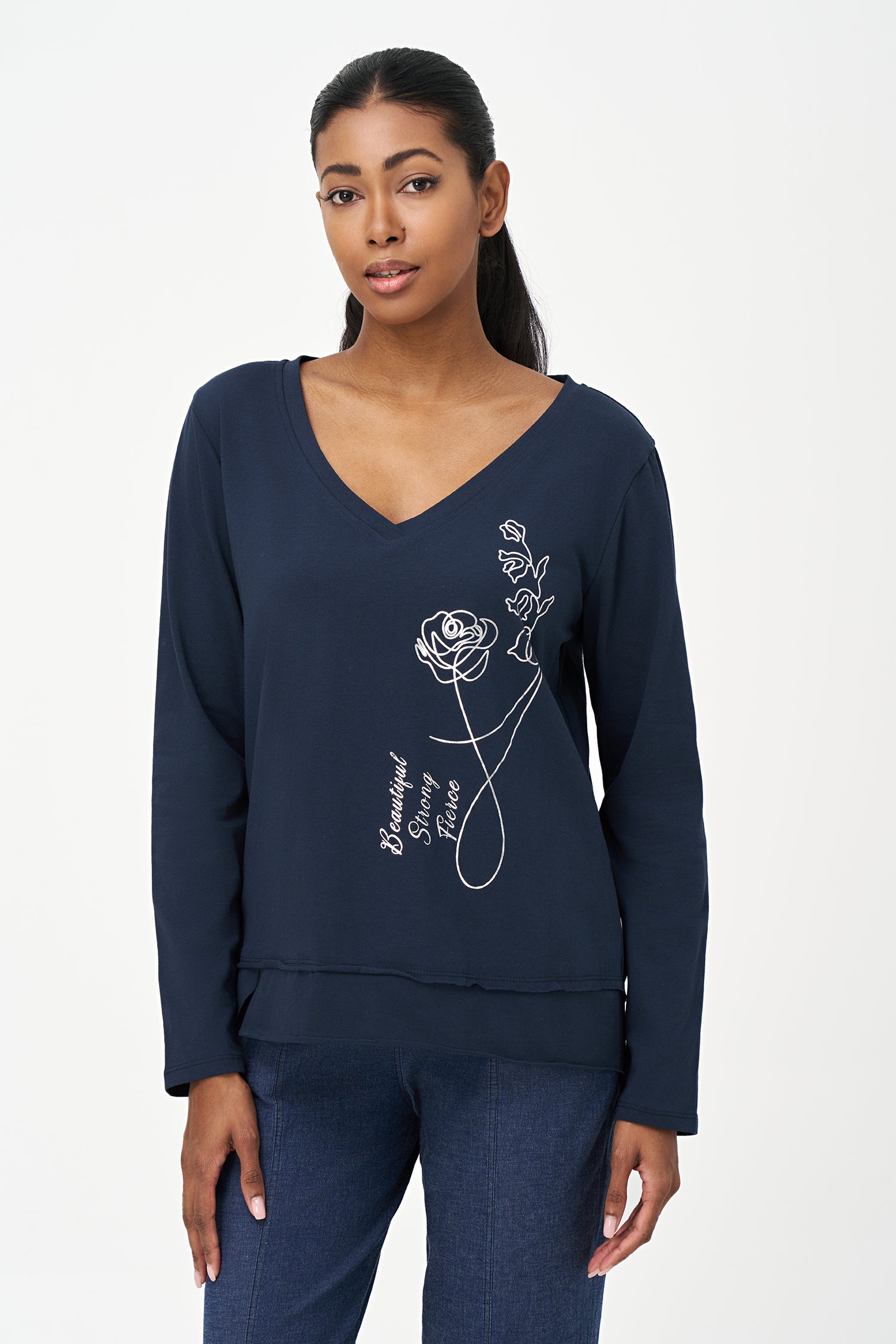 Blue V-neck long-sleeve top with white embroidered floral design and cursive script reading 'Beautiful, Bonjour, Fleur' on the front.