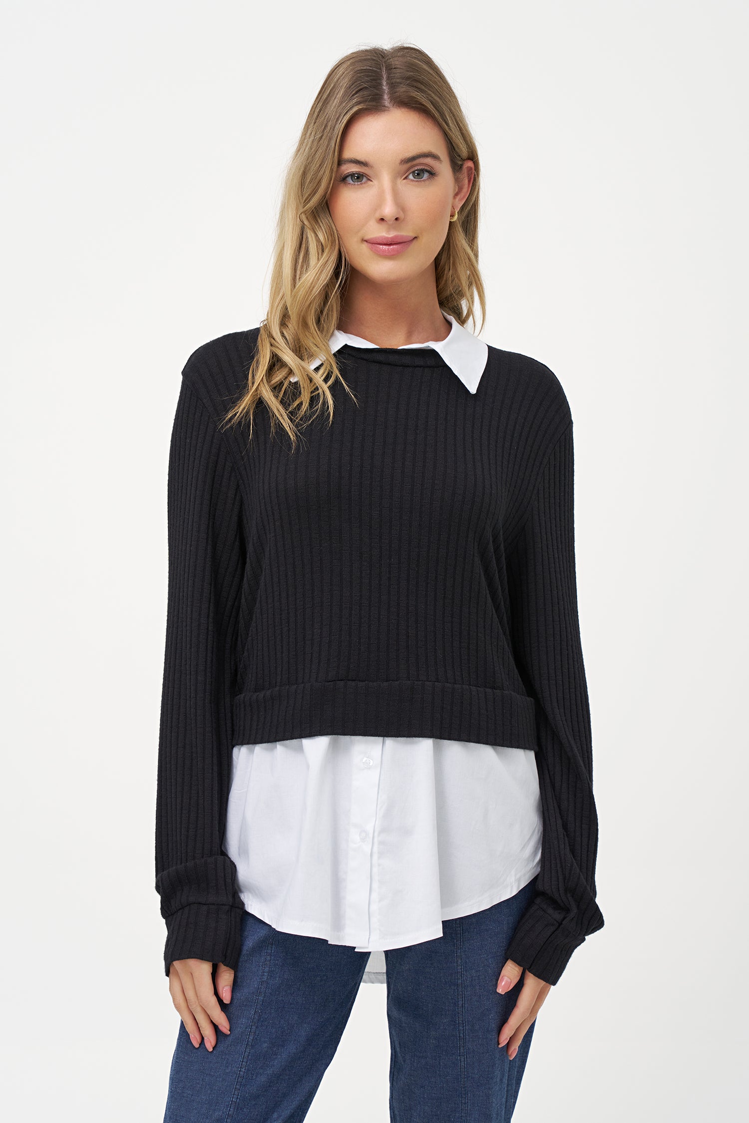 Black cashmere sweater layered over white blouse with long sleeves and curved hem.