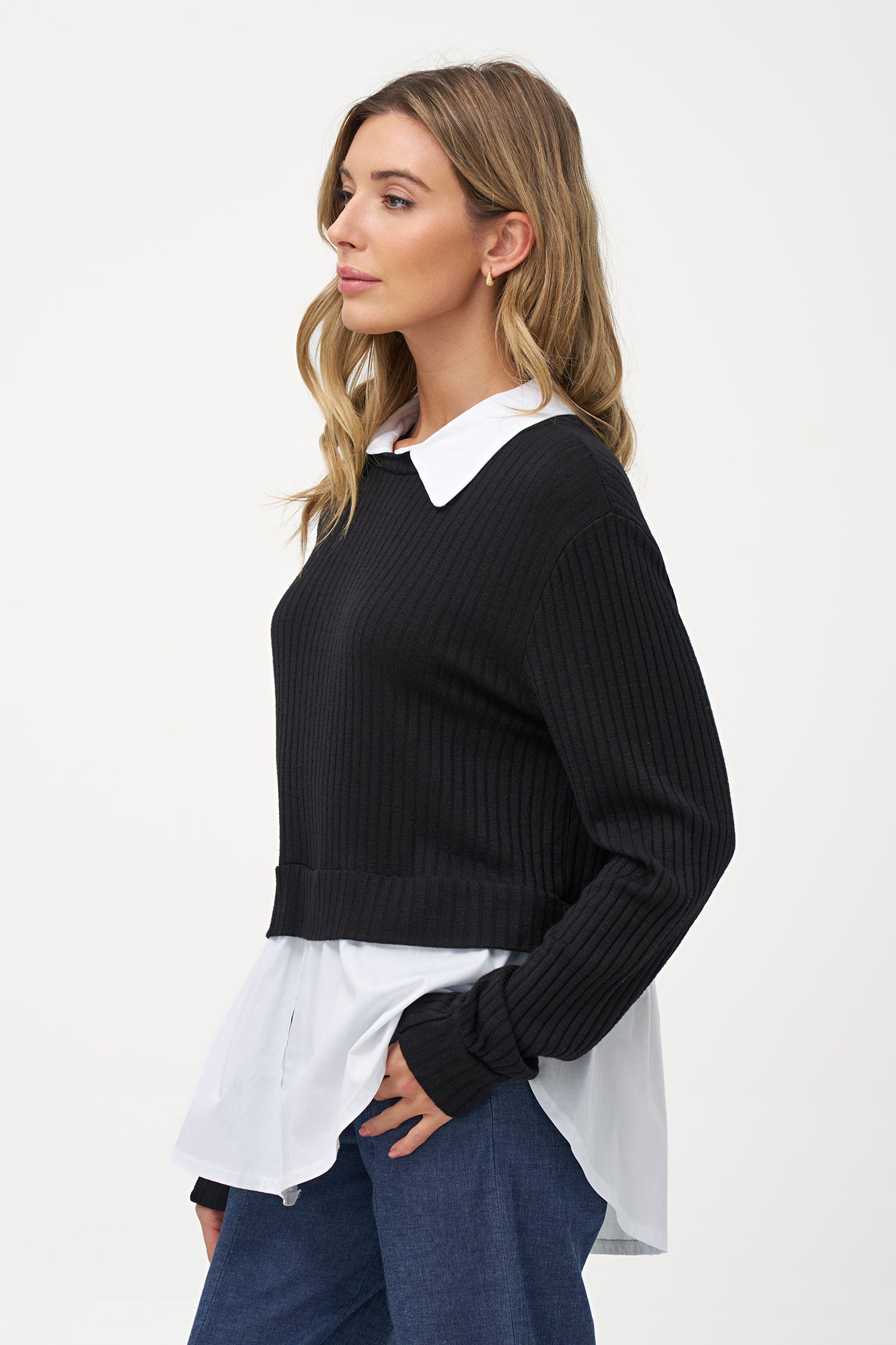 Black cashmere sweater layered over white blouse with long sleeves and curved hem.