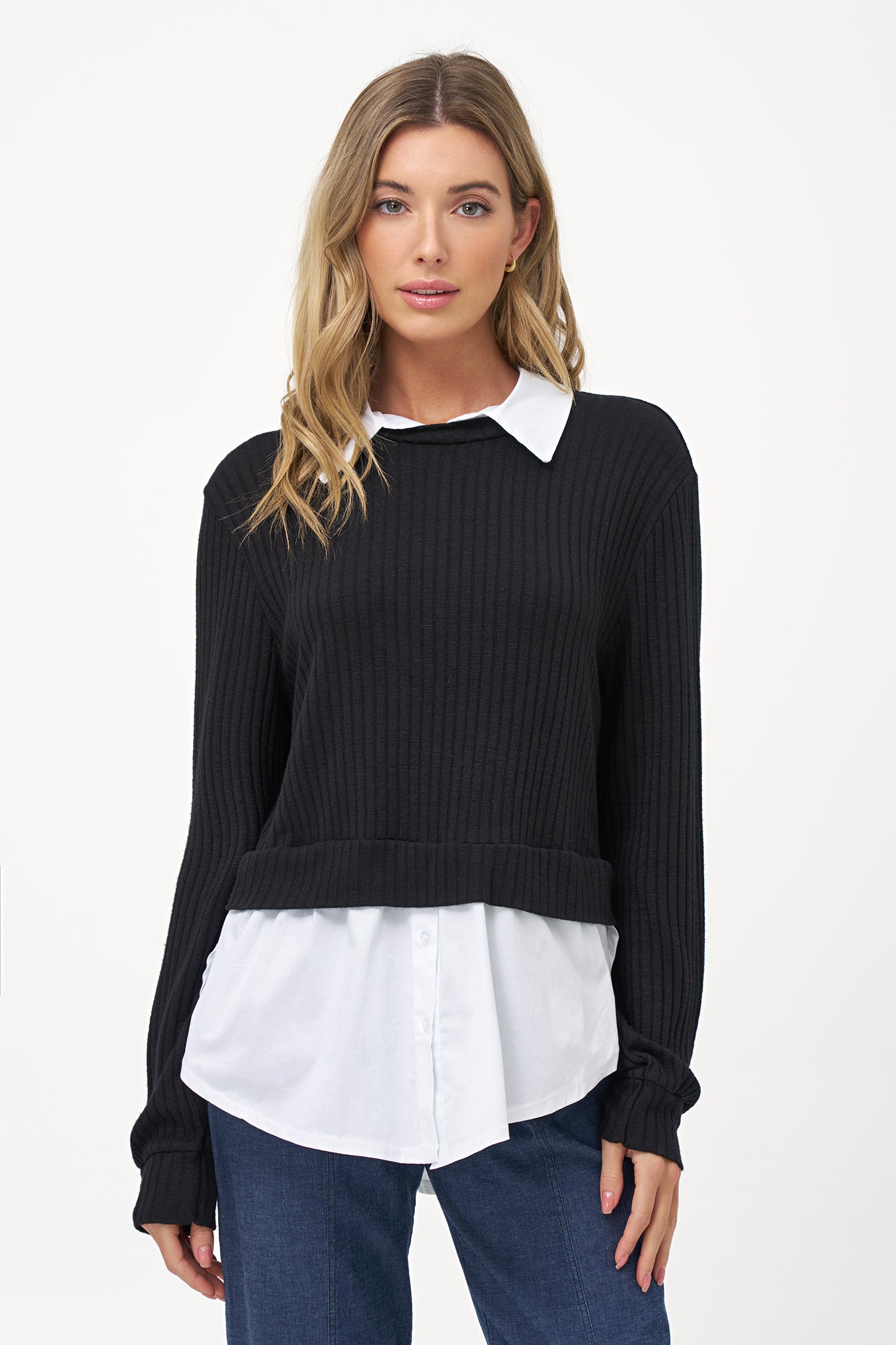 Black cashmere sweater layered over white blouse with long sleeves and curved hem.