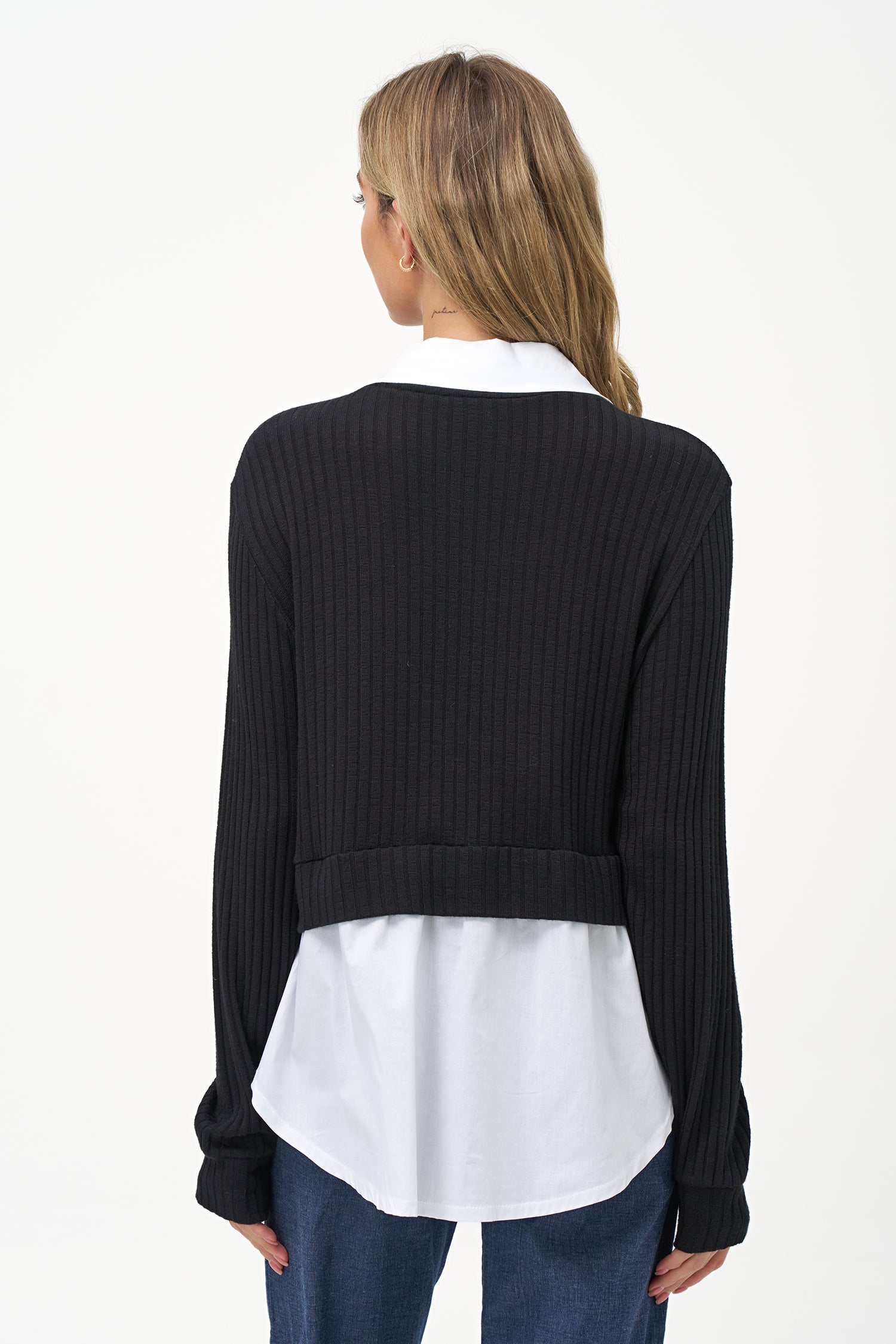 Black cashmere sweater layered over white blouse with long sleeves and curved hem.