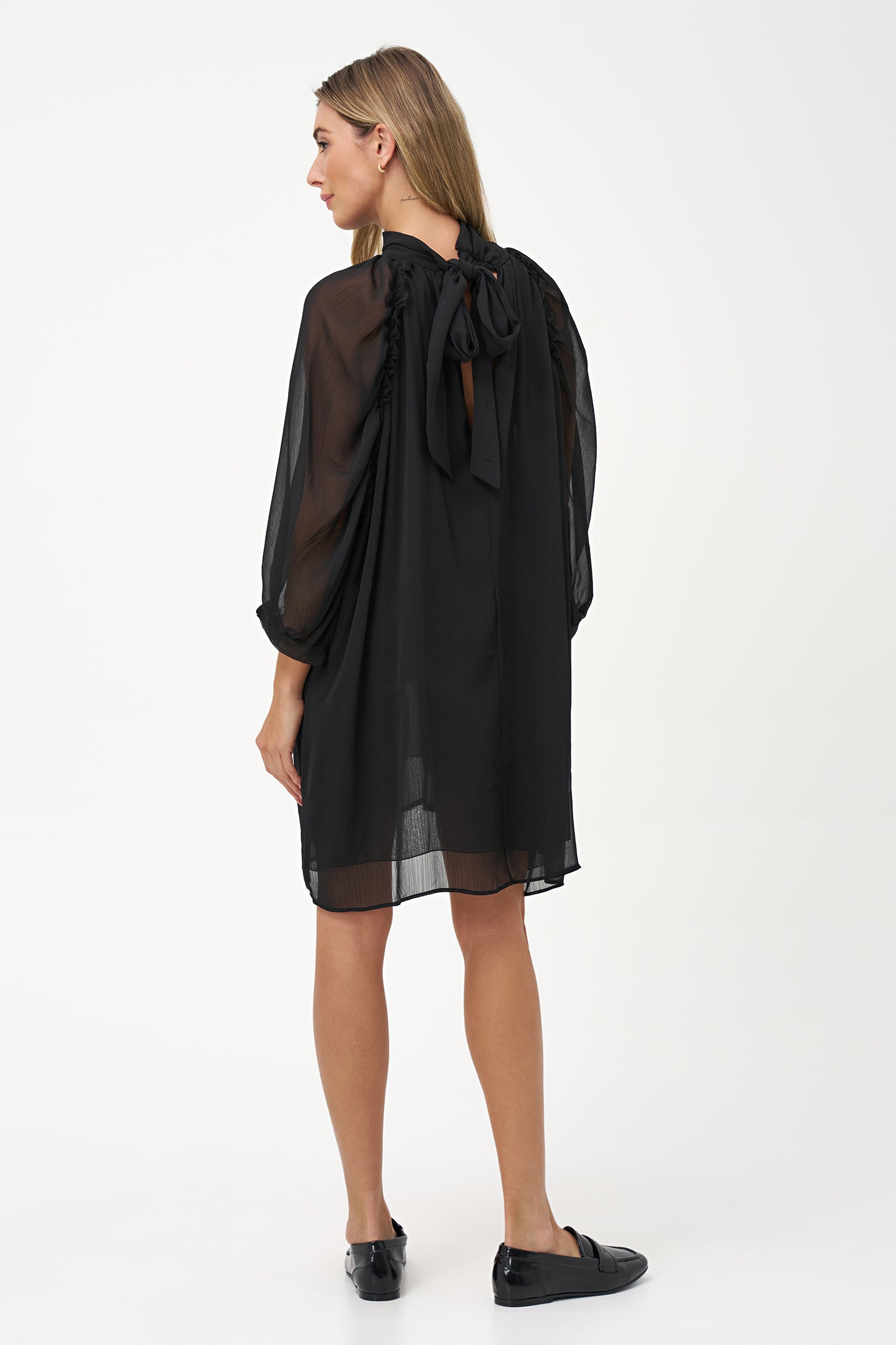 Sheer long-sleeve black dress with high neck and oversized bow detail.