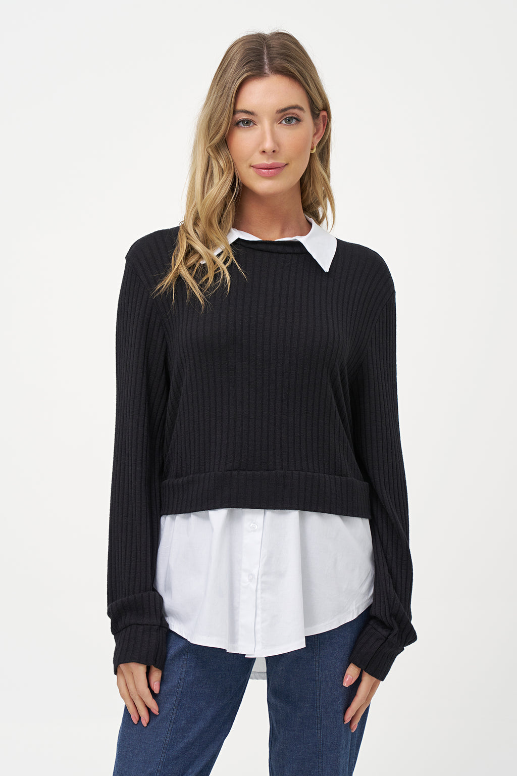 Black cashmere sweater layered over white blouse with long sleeves and curved hem.