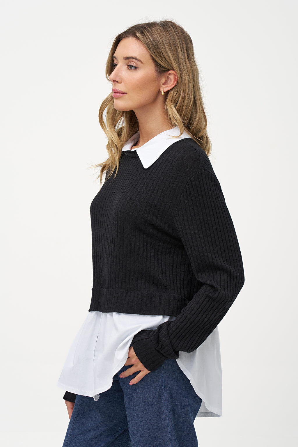 Black cashmere sweater layered over white blouse with long sleeves and curved hem.