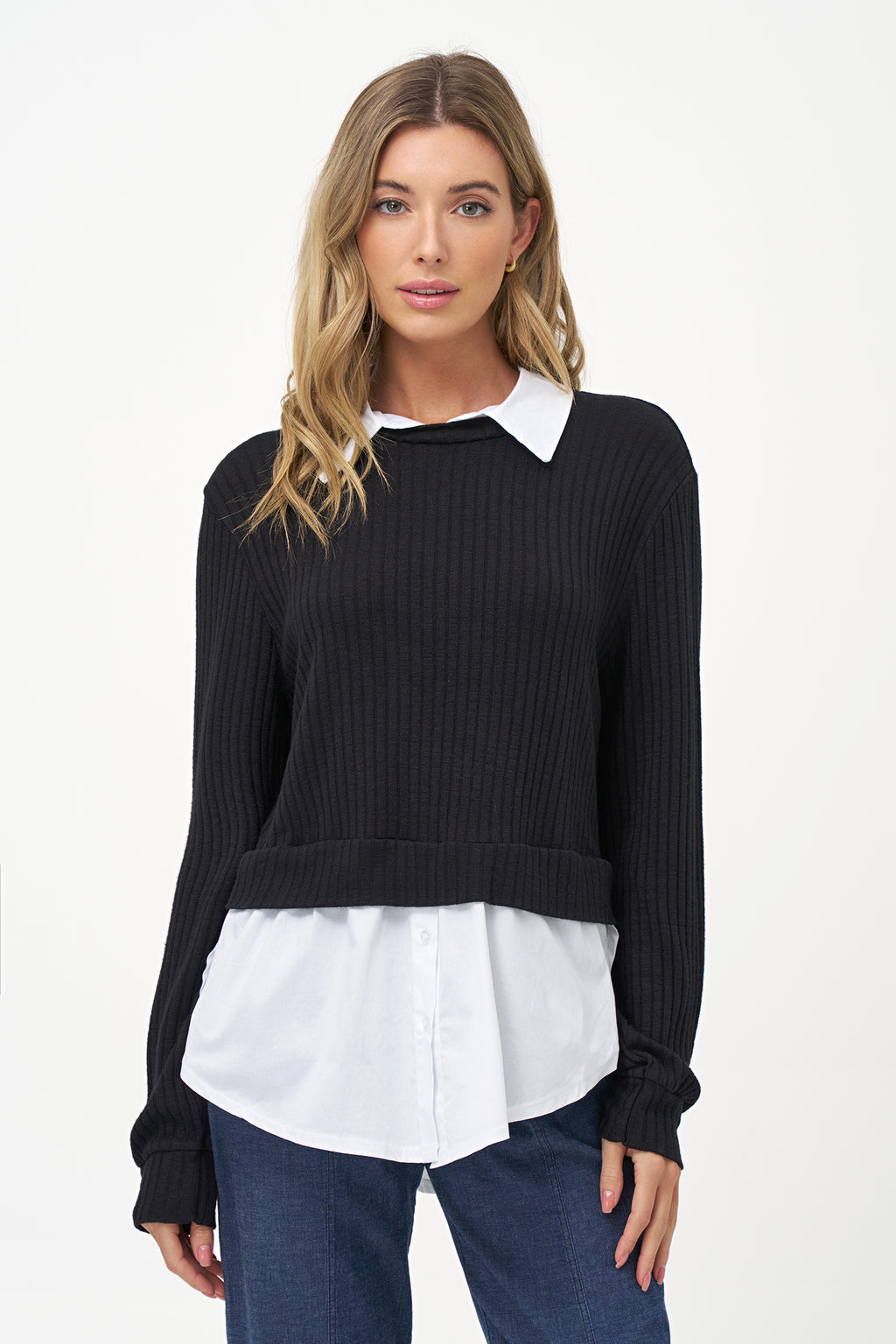 Black cashmere sweater layered over white blouse with long sleeves and curved hem.